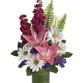 Pink lilies, white daisies, and purple flowers in a clear glass cylinder vase