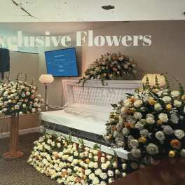 White and peach rose casket spray with matching floral pieces around a white casket