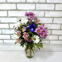 Mixed bouquet of pink, white, and blue flowers in a clear glass vase