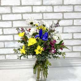 Mixed bouquet of yellow, white, blue, and purple flowers in a clear glass vase
