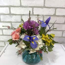 Mixed bouquet in a teal glass vase with pink roses, purple blooms, and blue iris