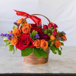 Basket arrangement of red and orange roses with purple accents