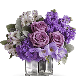 Purple and pink floral arrangement in a clear square vase