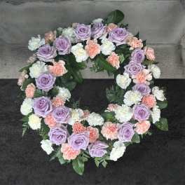 Circular floral wreath with lavender roses, white carnations, and peach carnations