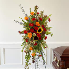 Standing funeral spray with orange and red flowers beside a casket