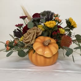 Autumn floral arrangement in a pumpkin-shaped container with mixed blooms