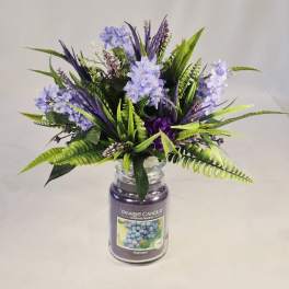 Purple and lavender floral arrangement in a glass jar candle container