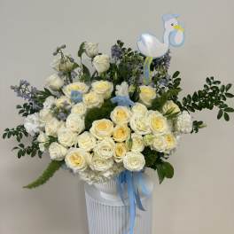 White and pale yellow roses in a vase with blue ribbon and a stork topper