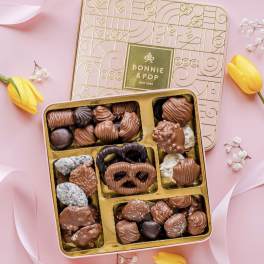 Box of assorted chocolates with yellow tulips on a pink background