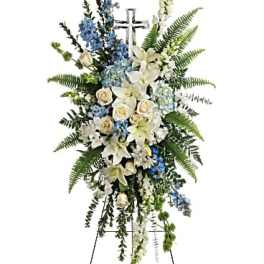 Standing funeral spray with white lilies, blue flowers, and a cross
