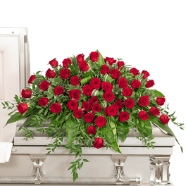 Red rose casket spray with cascading greenery on a white casket