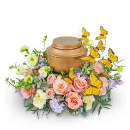 Peach and lavender floral arrangement around a bronze urn with butterfly picks
