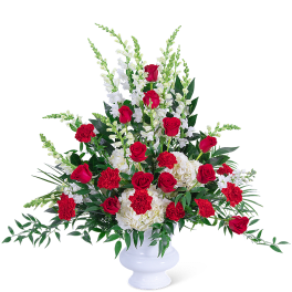 Red roses and white flowers arranged in a white pedestal vase