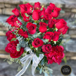 Tall arrangement of red roses and red peonies with a white bow