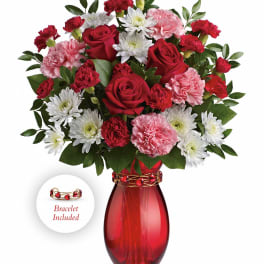 Red, pink, and white bouquet with roses and carnations in a red glass vase with bracelet accent