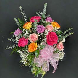 Mixed arrangement of pink, peach, lavender, and yellow roses with white filler flowers and a pink ribbon bow