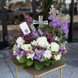 White roses and purple flowers arranged around a silver cross
