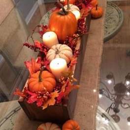Pumpkins and white candles arranged in a long wooden tray