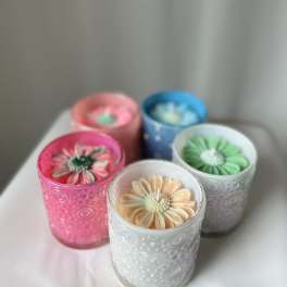 Five flower-shaped candles in colored glass holders on a table