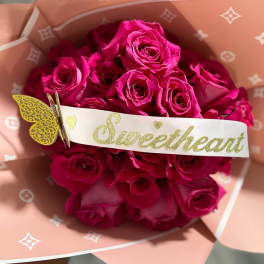 Bouquet of bright pink roses wrapped in peach paper with a Sweetheart tag