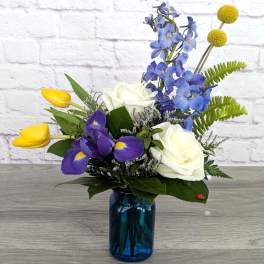 Bouquet of white roses, blue flowers, and yellow tulips in a blue glass vase