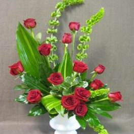 Red roses arranged in a white vase with tall green foliage