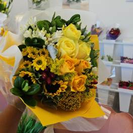 Yellow rose bouquet with white flowers and green accents wrapped in paper