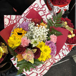 Mixed bouquet with roses, daisies, carnations, and baby's breath in red wrapping
