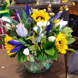 Mixed bouquet with sunflowers, purple tulips, and pale roses in a glass vase