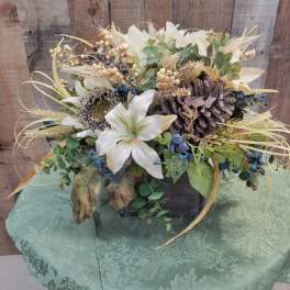 White lily arrangement with pinecones and berries in a dark container