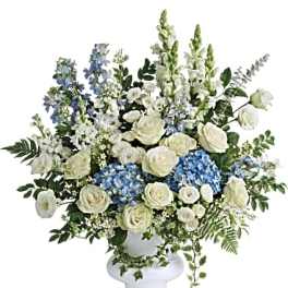White roses and blue flowers arranged in a white pedestal vase