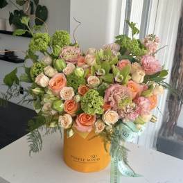 Mixed bouquet of peach and pink roses with green blooms in an orange hatbox