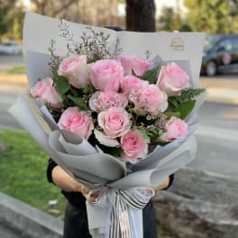 Handheld bouquet of pink roses wrapped in gray paper with ribbon