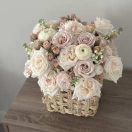 Pastel roses and ranunculus arranged in a woven basket