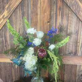 Mixed floral arrangement in a clear glass vase with white, blue, and green blooms