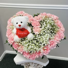 Heart-shaped pink carnation arrangement with a teddy bear holding a red heart