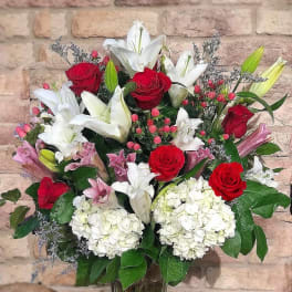 Tall bouquet of red roses, white and pink lilies, and white hydrangeas in a clear glass vase