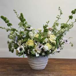 Low floral arrangement in a textured white pot with pale roses and white blooms