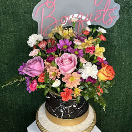 Mixed bouquet in a black round box with pink sign behind it