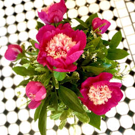 Pink peony bouquet with green foliage on a tiled surface