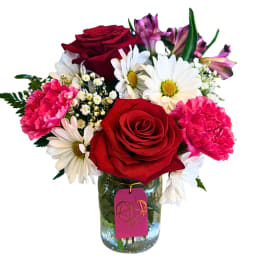 Bouquet of red roses, pink carnations, and white daisies in a glass jar