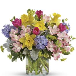 Mixed bouquet of daffodils, tulips, alstroemeria, and blue flowers in a glass vase