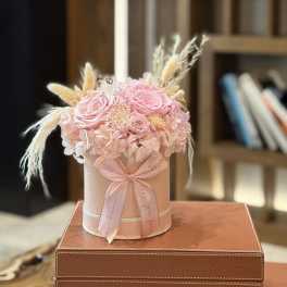 Pink roses and hydrangeas arranged in a round hatbox with a ribbon