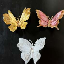 Three decorative butterfly ornaments in gold, pink, and white on a black background