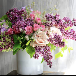 Pink roses and purple lilacs arranged in a white vase