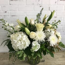 White hydrangeas, roses, lilies, and mums arranged in a clear glass vase