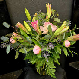 Pink lilies and peonies arranged in a glass vase with greenery.