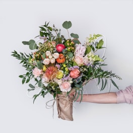Handheld bouquet of mixed pink and peach flowers with greenery