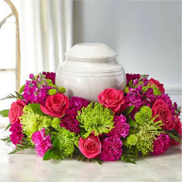 Pink roses and magenta flowers arranged around a white urn