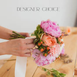 Handheld bouquet of pink and peach flowers with a white ribbon